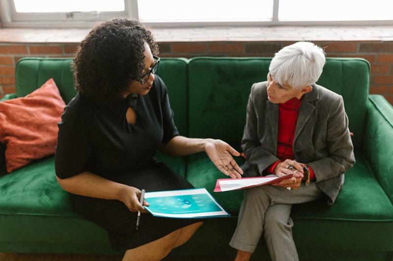 Two women on a sofa look over papers together.