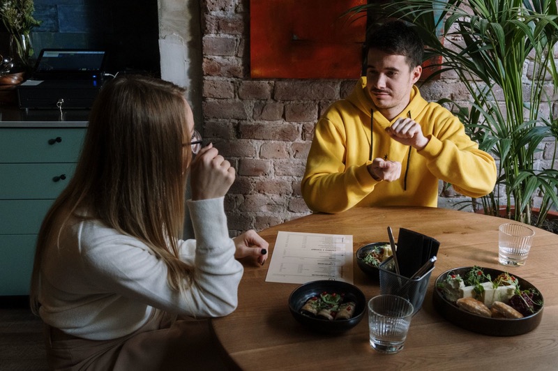 Two friends talk in sign language over lunch.