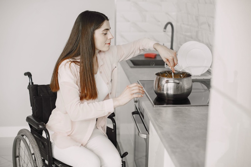 A woman in a wheelchair stirs a pot on the stove.
